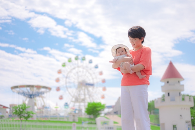 遊園地前で赤ちゃんを抱っこしているオレンジ色のシャツの母親