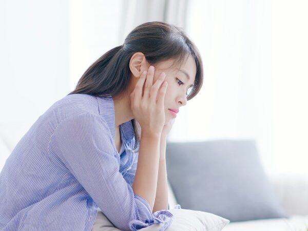 ソファーで頬杖ついて考えている女性