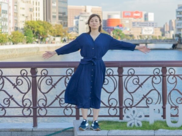 濃紺のワンピースを着て目を閉じて両手を広げている女性