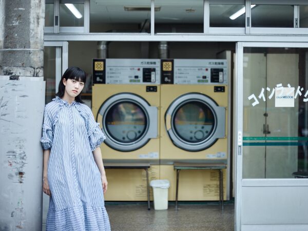 黄色いコインランドリーとコインランドリー前に立つ女性