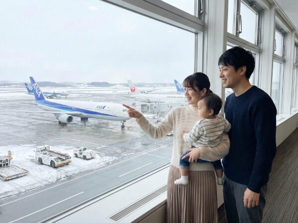 空港内から外の飛行機を見て指をさしている3人家族