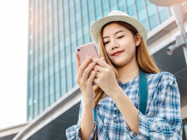 旅行中にスマホを見ている白い帽子と青いチェック柄の服の女性